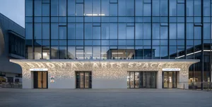 Modern building exterior featuring glass walls, concrete structures, and illuminated lighting at dusk