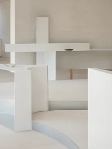 A minimalist interior space with white and concrete elements, featuring a curved staircase and minimal decor.