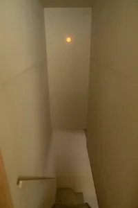 A minimalist staircase made of concrete and glass, illuminated by a singular light source.