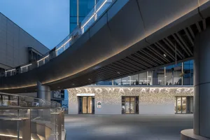 An exterior view of a modern shopping center featuring concrete materials, illuminated pathways, and sleek architectural line