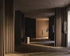 A minimalist clothing boutique featuring draped curtains and exposed ceiling lights.