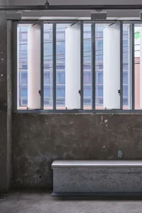 Minimalist white window with metal frame on a concrete floor with a bench.