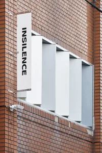 A white sign with the word 'INSILENCE' is mounted on a brick wall.