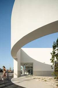 A minimalist storefront with a curved concrete facade and large glass windows.
