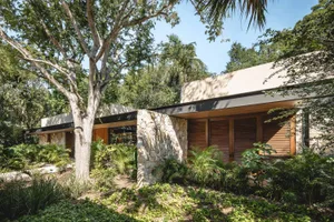 A modern house with a stone exterior surrounded by lush greenery and trees.
