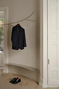Modern metal and stone wall-mounted clothing hanger with a navy-blue blazer hanging on it, near a pair of black shoes on the 