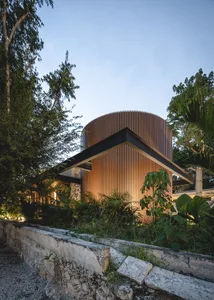 A modern minimalist roundhouse with a wooden exterior and marble flooring at dusk.