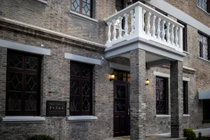 A daytime photograph of an urban brick building with decorative white columns and wall-mounted lamps in front of the entrance