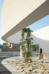A woman walks past a modern entryway featuring a tree planted in a bed of concrete and glass tiles.