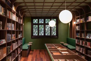 現代圖書館室內，配有木質書架、綠色座椅，以及帶有菱形窗格的大窗戶。