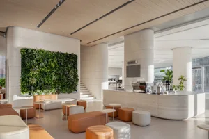 A modern, minimalist coffee shop lobby with a white concrete floor, white and orange seating areas, and a green living wall.