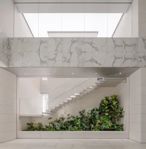 A modern and minimalist interior space with marble walls and floors, featuring a glass ceiling and green plants.