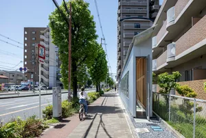 A modern urban sidewalk with high-rise buildings on either side and a cyclist riding on the pathway.