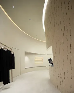 A minimalist retail store interior with concrete walls and flooring, featuring a black clothing rack and illuminated shelves.