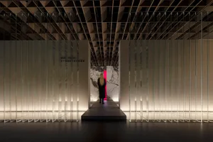 A modern exhibition space featuring a glass-walled corridor and a white marble wall with a red accent.