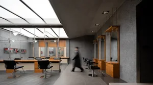 A modern salon interior featuring sleek concrete flooring and walls, with black chairs and illuminated ceilings.