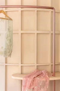 Clothing displayed on a modern metal hanger and stand against a paneled wall.