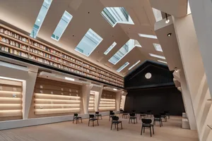 現代圖書館室內空間，木質牆面、高挑天花板搭配天窗，以及中央舞台周圍排列的座椅