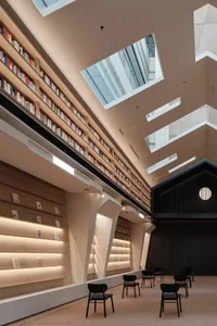 現代圖書館室內，木質書架、玻璃牆面與混凝土天花板搭配天窗。