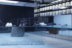Retail store featuring various footwear displays including glass tables, metal shelves, stone bases, and concrete flooring.