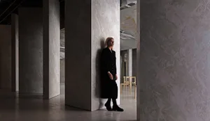 A person standing in a minimalist interior with concrete walls.