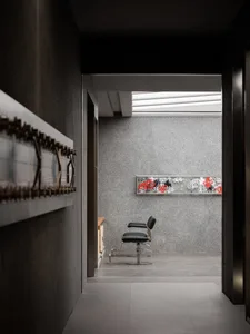 A minimalist barber shop interior featuring a concrete wall with a black and red graffiti piece above a black barber chair.