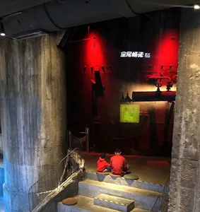 Two individuals seated on a step in a museum exhibit featuring concrete pipes and a painting with red lighting.