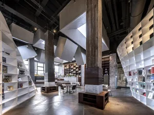A spacious, industrial-style library with concrete walls and floor, featuring modern furniture and an open, airy design.