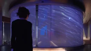 A person stands in front of a large, digital projection screen displaying an abstract design with a starry, space-themed back
