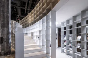 A modern, minimalist interior featuring a concrete and steel structure with a spiral staircase and a bookshelf.