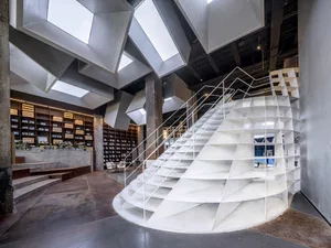 A contemporary library with a spiral staircase made of concrete and glass.