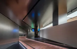 A sleek, modern corridor with metal-clad walls and a concrete floor, illuminated by contemporary lighting.