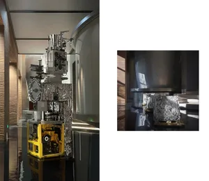 A complex, metallic machine with various components and equipment, reflected on a glossy, reflective surface in a spacious, m