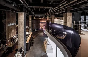 A modern industrial coffee shop bar with exposed concrete walls, wooden furniture, and large windows.
