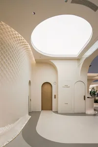 A minimalist lobby interior featuring textured plaster walls and a concrete floor with a circular skylight and arched doorway