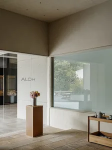 A minimalist modern coffee shop interior with concrete walls and flooring, featuring a coffee service cart and floral arrange