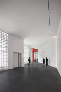 A spacious, minimalist lobby with a concrete floor and walls, featuring large windows.