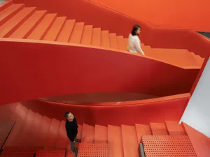 A modern red staircase interior design with a person standing on the lower steps and another walking up the upper steps.