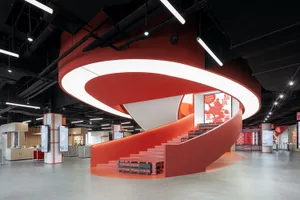 A modern industrial retail space featuring a red concrete spiral staircase with a curved railing.