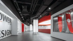A minimalist exhibition space with red accents, white walls, and black ceiling pipes.