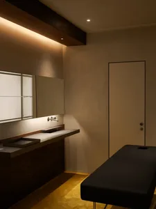 Modern minimalist medical office room with concrete floor, wooden walls, and a black leather patient bed