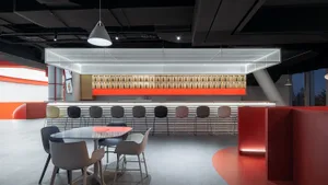 A modern bar interior with red accent walls, white concrete surfaces, and metal stools.