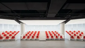 A modern conference room with red plastic seats arranged in rows with white railings.
