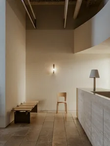 A minimalist modern reception space featuring wooden furniture and textured concrete walls.