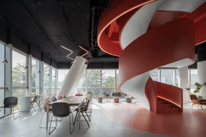 A modern office space featuring a red and white curved panel wall and a large table surrounded by chairs.