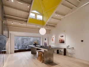 A modern office space featuring a metal and glass dining table with modern chairs and artwork.