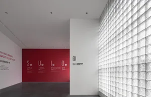 A modern event space with transparent glass block walls and red informational posters on a deep grey floor.
