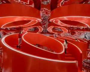 Two people standing on a spiral staircase surrounded by red metallic walls with neon lighting.