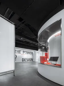 A minimalist exhibition space with white walls and a curved glass wall.