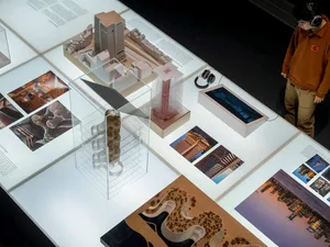 A display of architectural models and photographs in a museum or exhibition setting.